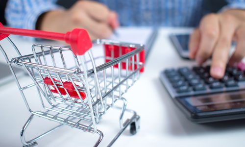  A person using a desktop calculator with a small shopping cart in the foreground.